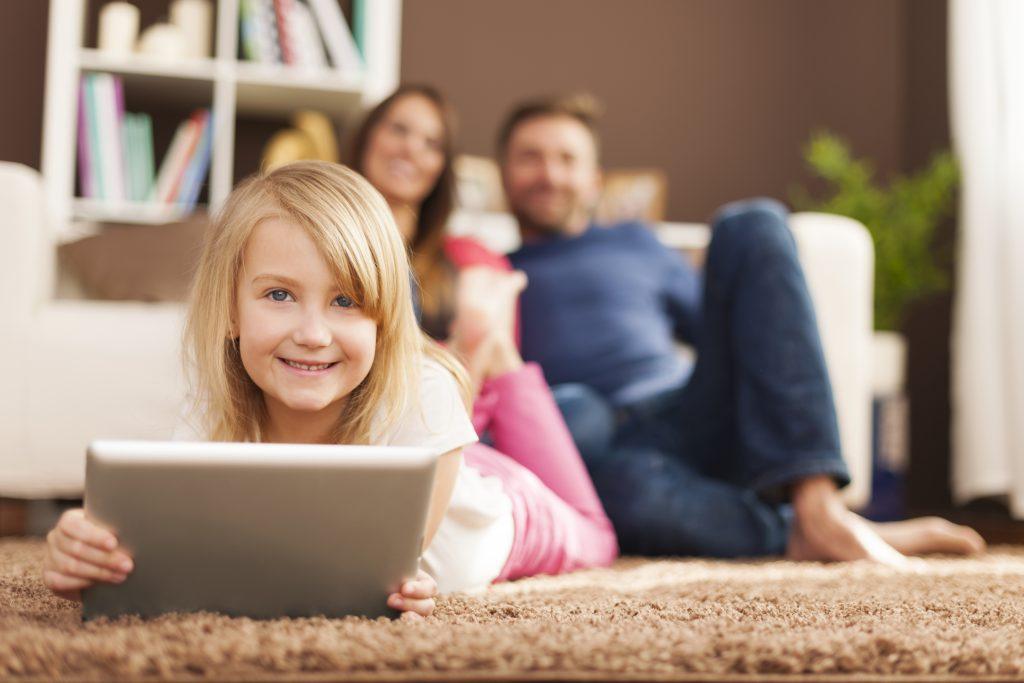 Smiling little girl playing on tablet and lying on carpet