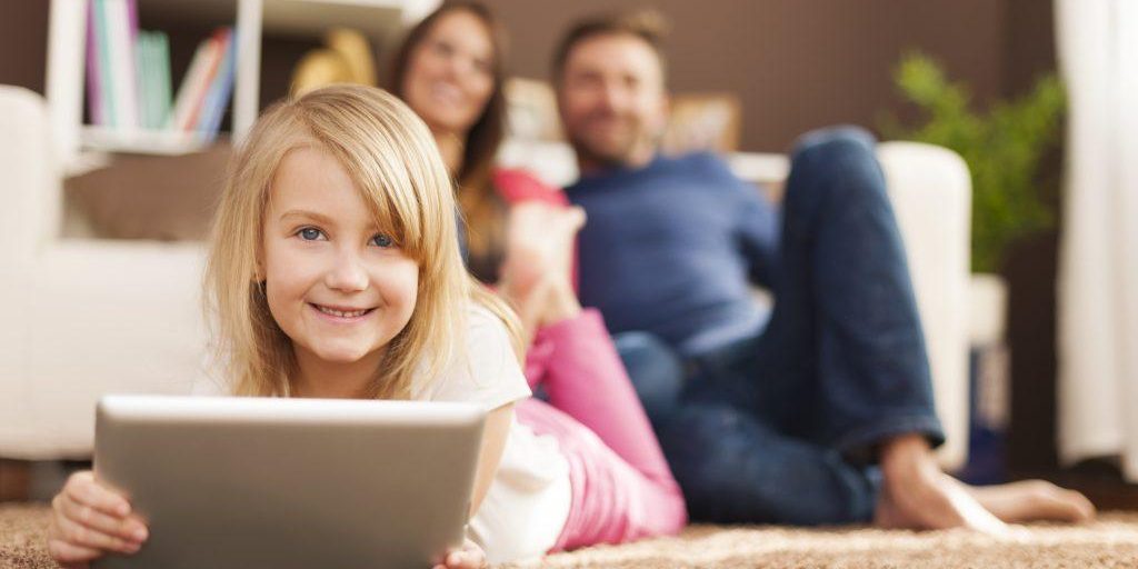 Smiling little girl playing on tablet and lying on carpet